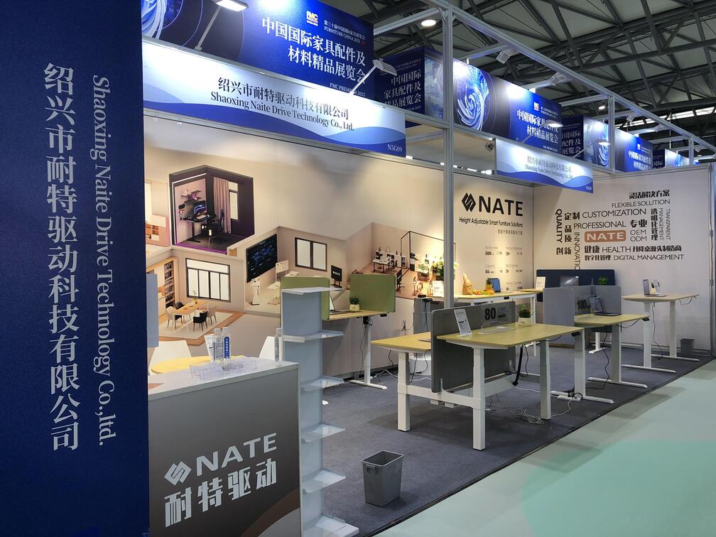 Wide-angle view of the Shaoxing Naite Drive Technology booth at the FMC Premium 2025 exhibition, showcasing a range of modern height-adjustable standing desks.