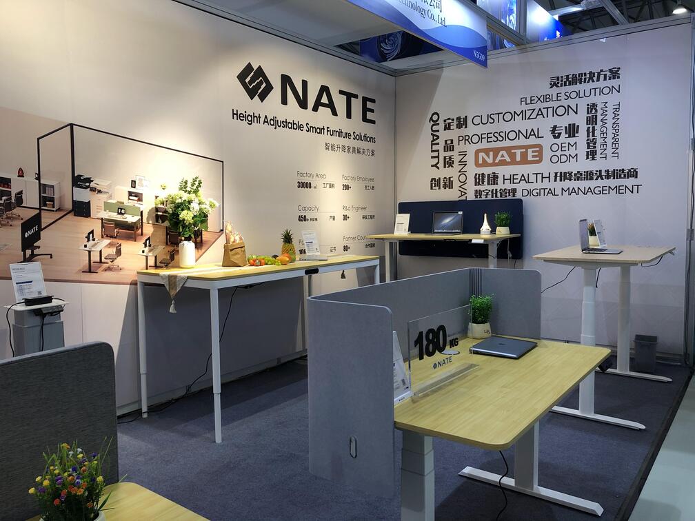 NATE's exhibition booth interior, featuring a standing desk demonstrating its 180kg load capacity and a display wall with company information.