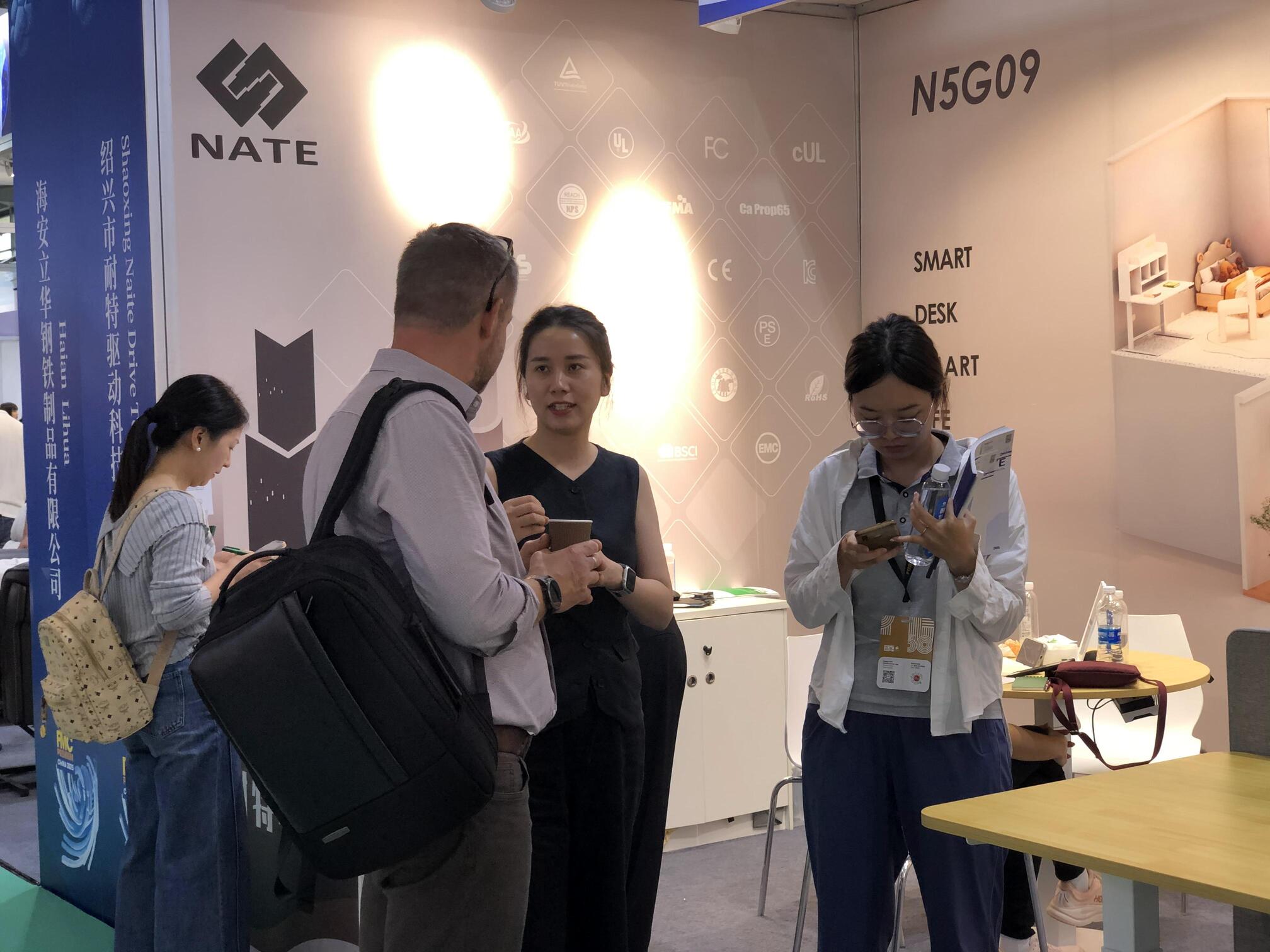 A NATE team member discusses product details with an international visitor at booth N5G09 during the FMC Premium 2025 trade show.