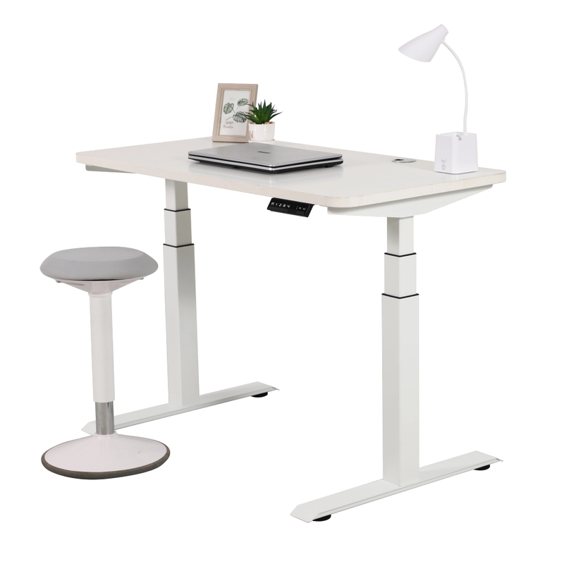 A white 2B3 adjustable standing desk with a white tabletop, set up with a laptop, small plant, and a desk lamp. A grey and white ergonomic stool is placed next to the desk, all against a white background.