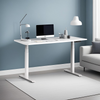 A complete white electric height-adjustable desk set up in a modern home office with a computer and lamp, showcasing its clean and minimalist aesthetic within a home environment.